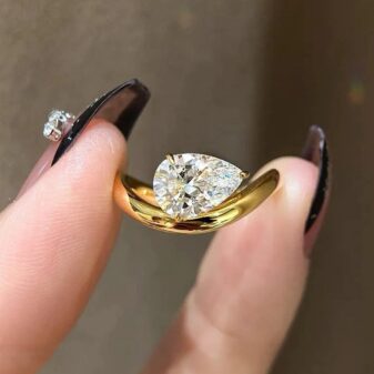 A brilliant pear-cut diamond floats within a unique, curved gold setting.